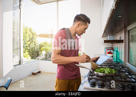 Young man following cooking instructions in kitchen Stock Photo