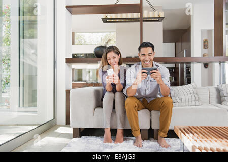 Couple playing games on smartphones on sitting room sofa Stock Photo