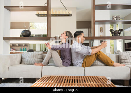 Couple sitting back to back playing games on smartphones on sitting room sofa Stock Photo