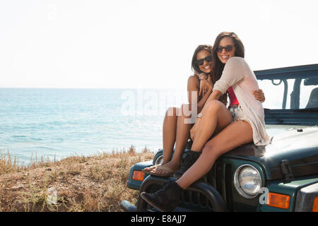 Portrait of two young women sitting on jeep hood at coast, Malibu, California, USA Stock Photo