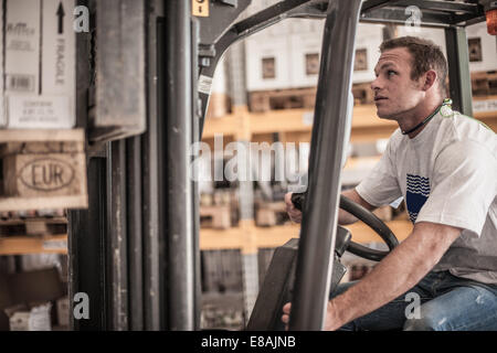 Young man driving forklift truck in factory warehouse Stock Photo