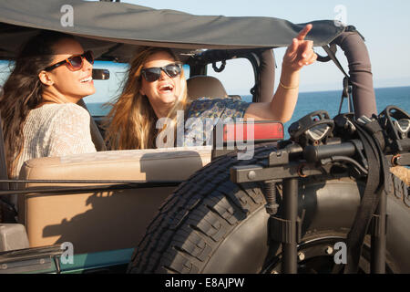 Two young women looking up from jeep at coast, Malibu, California, USA Stock Photo