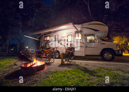 Mid adult couple and baby daughter sitting in front of campfire at night Stock Photo