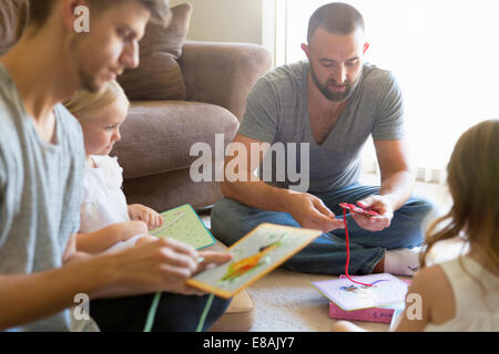 Male couple and two daughters threading picture books on sitting room floor Stock Photo