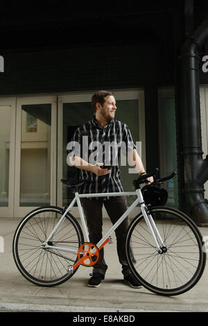 Male cycle messenger checking directions on smartphone outside office