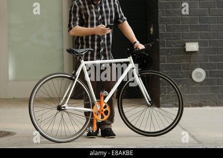 Neck down view of male cycle messenger checking directions on smartphone outside office
