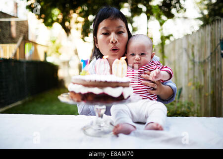 Mother holding baby son, blowing out candles on cake Stock Photo