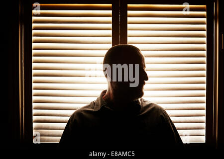 Portrait of silhouetted mature man in front of window blind Stock Photo