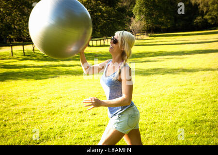 Young woman playing around with exercise ball in field Stock Photo