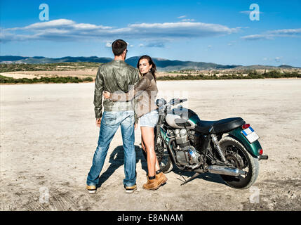 Rear view of young couple and motorcycle on arid plain, Cagliari, Sardinia, Italy Stock Photo