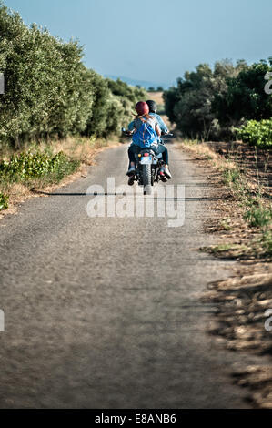 Rear view of mid adult couple riding motorcycle on rural road, Cagliari, Sardinia, Italy Stock Photo