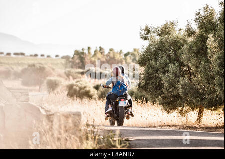 Rear view of mid adult couple riding motorcycle on dusty rural road, Cagliari, Sardinia, Italy Stock Photo