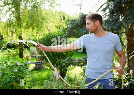 Mid adult man watering garden with hosepipe Stock Photo