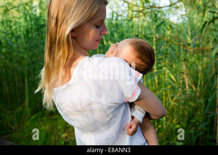 Rear view of mid adult mother and sleeping baby daughter in garden