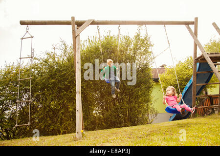 Brother and sister playing on swings in garden Stock Photo