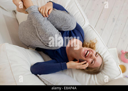 Woman lying on sofa laughing on smartphone Stock Photo