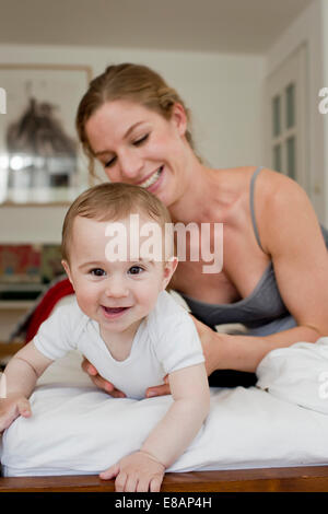Mother guiding baby boy crawling on bed Stock Photo