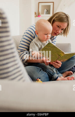 Mature mother reading storybook to baby daughter on sitting room sofa Stock Photo