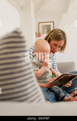 Mature mother and baby daughter reading storybook on sitting room sofa Stock Photo