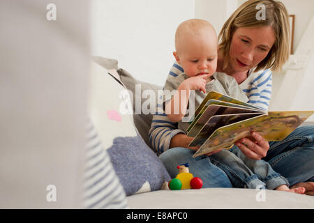 Mature mother and baby daughter on sitting room sofa reading storybook Stock Photo