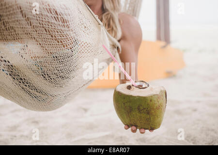 Man enjoying coconut water in hammock on beach Stock Photo