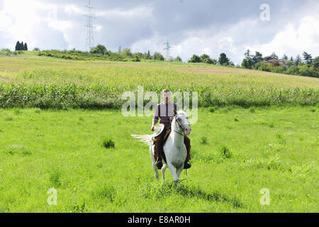 Young man holding cowboy hat galloping on horse in field Stock Photo