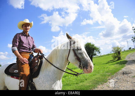 Portrait of young man in cowboy gear on horse on rural road Stock Photo