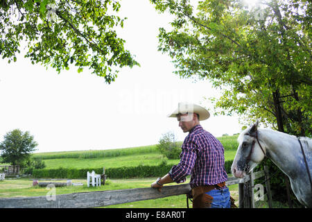 Young man in cowboy gear with horse checking fence Stock Photo