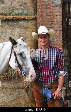 Portrait of young man in cowboy gear with horse outside stable Stock Photo