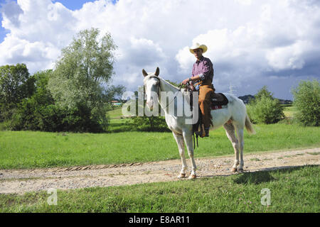 Portrait of young man in cowboy gear on horseback on dirt track