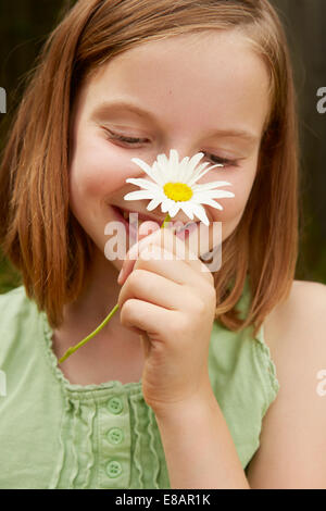 Portrait of girl in garden holding up daisy