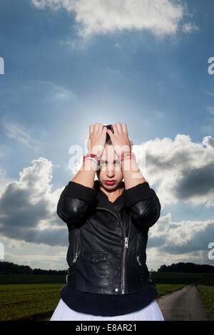 Portrait of young woman on rural road with head in hands Stock Photo