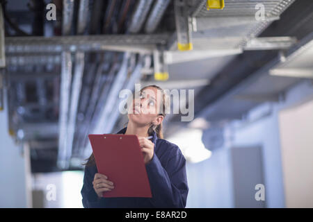 Female engineer with clipboard checking industrial piping in factory Stock Photo
