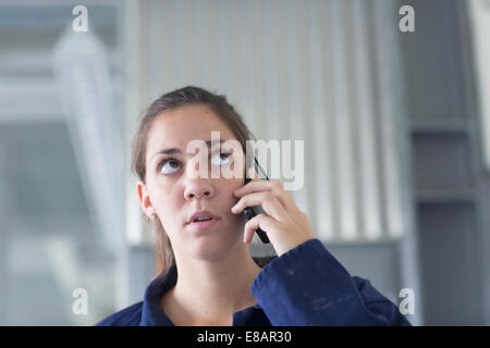 Worried female engineer talking on smartphone in factory Stock Photo