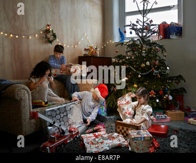 Sisters and brothers opening christmas gifts in sitting room Stock Photo