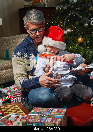 Father on sitting room floor opening christmas gifts with son Stock Photo