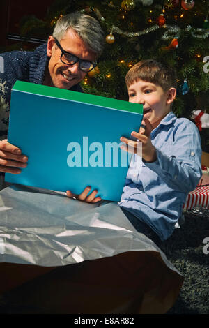 Father on sitting room floor opening christmas gifts with son Stock Photo