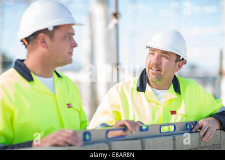 Builder and site manager using spirit level on construction site wall