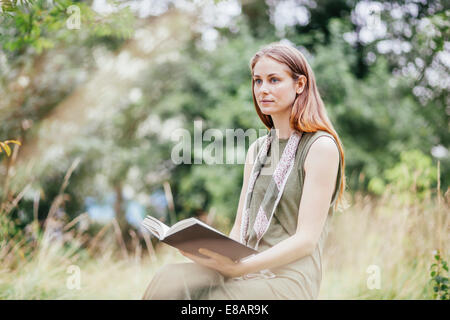 Young woman in field distracted from reading book Stock Photo