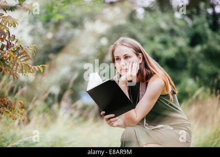 Young woman with chin on hand reading book in field