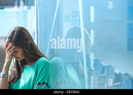 Mid adult businesswoman leaning against glass wall in office with hand on face Stock Photo