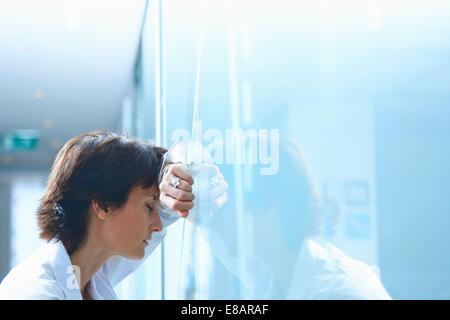 Mature businesswoman with eyes closed leaning against glass wall in office Stock Photo