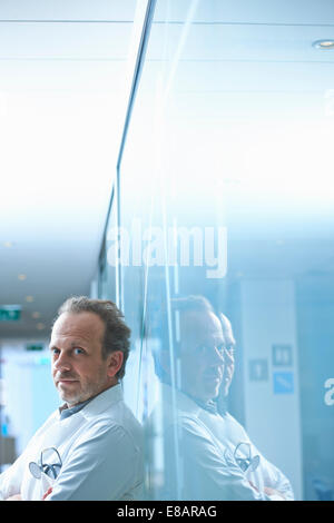 Portrait of mature businessman leaning against glass wall in office Stock Photo