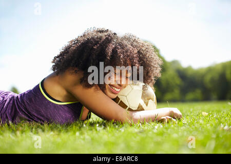 Young woman taking a break in park leaning on football