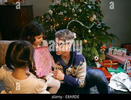 Father and two daughters opening christmas gifts in sitting room Stock Photo