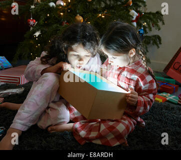 Two sisters open mouthed on unwrapping glowing christmas gift box Stock Photo