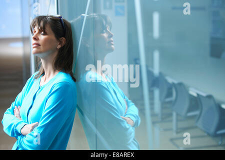 Mature businesswoman leaning against glass wall in office with eyes closed Stock Photo