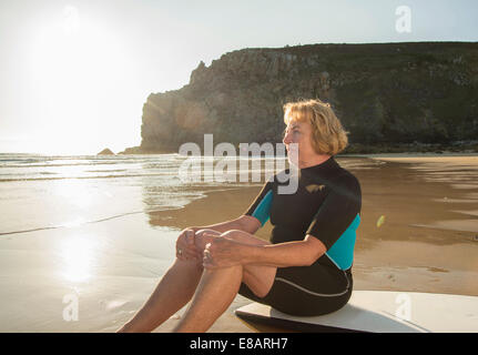 Senior woman surfer sitting on surfboard, Camaret-sur-mer, Brittany, France Stock Photo