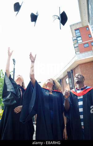 Three college students throwing graduation caps mid air Stock Photo