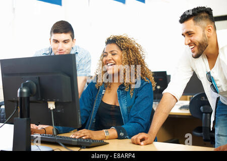 Three student friends laughing and looking at personal computer in classroom